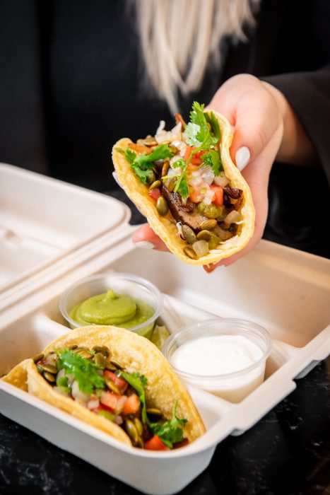 Hand holds Mushroom Tacos about takeout container